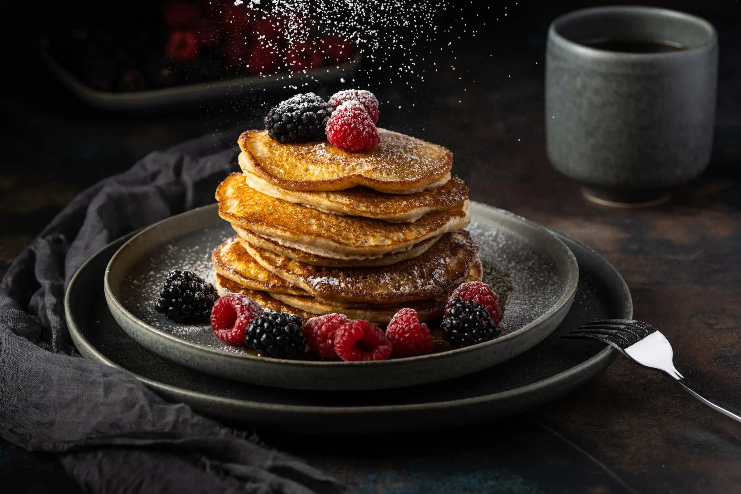 A stack of pancakes with raspberries and blackberries, dusted with sugar