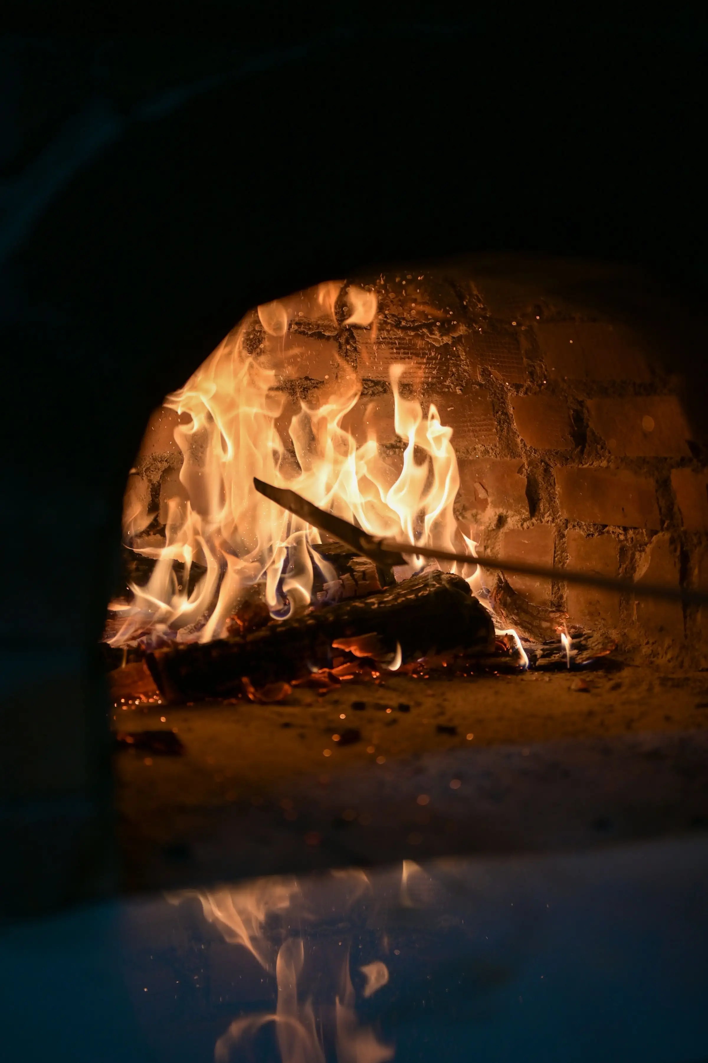 A peel resting in the mouth of the brick oven as the fire burns