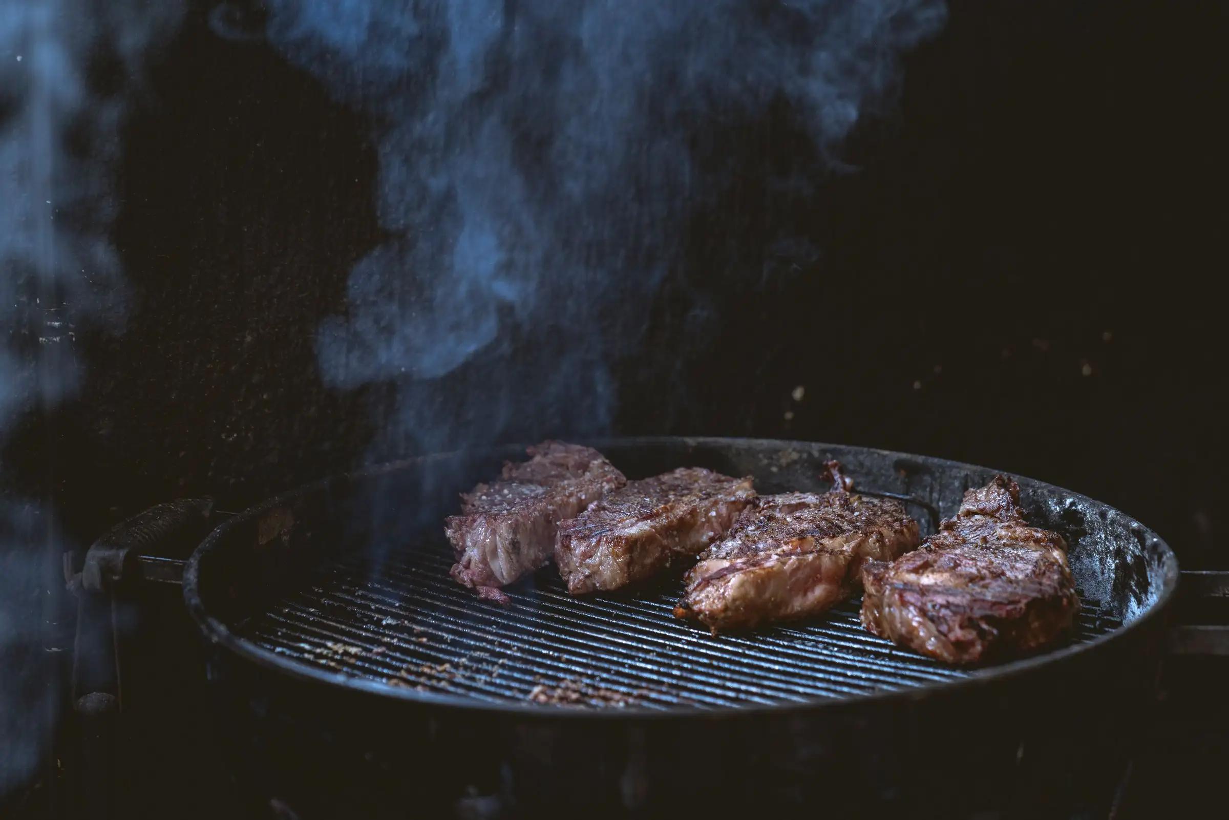 Thick-cut steaks resting on a grill over glowing coals, smoke rising around them