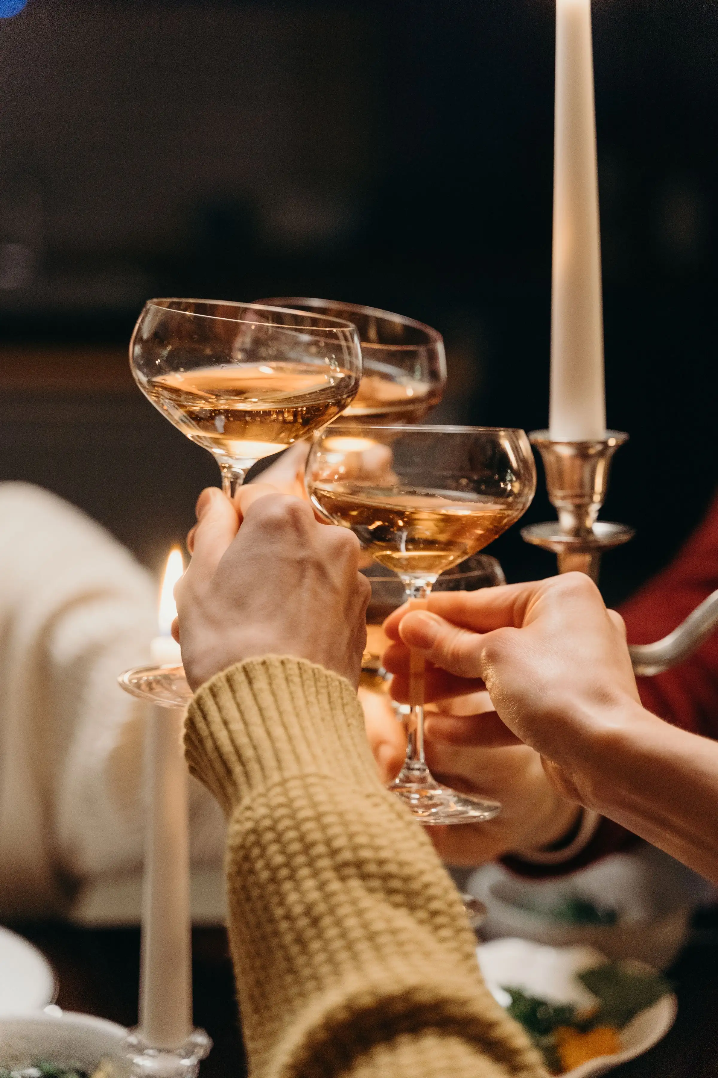 Guests raising coupe glasses together in a candlelit toast